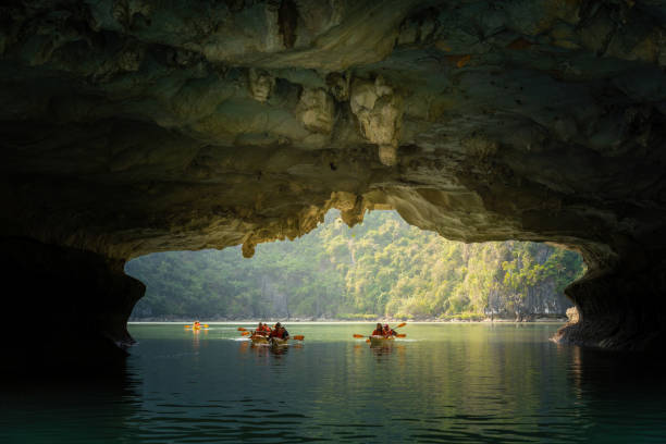 blick auf touristen, die die ruhige tropische bucht mit kalksteinbergen mit dem kajak erkunden. leben, leute und natur in ha long bay, vietnam - halong bay stock-fotos und bilder