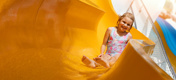 happy little girl on slide at outdoor water park. banner with copy space