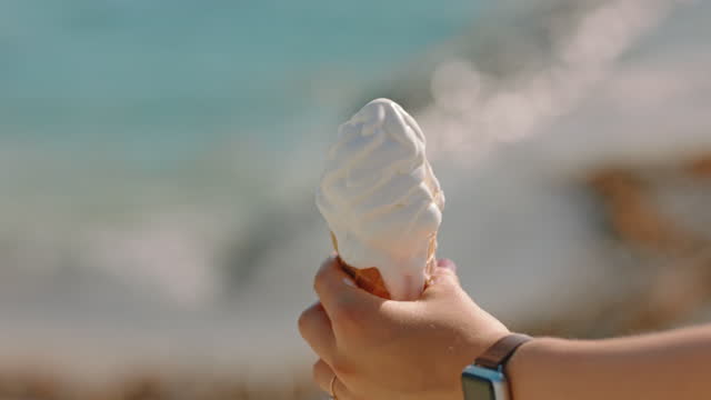 close up hand woman holding ice cream vanilla flavored dessert on beatiful sunny beach enjoying summer vacation eating soft serve