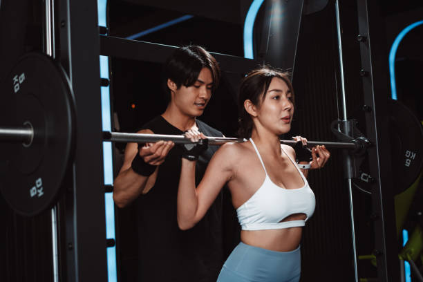 Woman working out Bodybuilder with coaching assistance to support weights at the gym. bodybuilder doing exercises with barbell. training sport healthy lifestyle bodybuilding. Woman working out Bodybuilder with coaching assistance to support weights at the gym. bodybuilder doing exercises with barbell. training sport healthy lifestyle bodybuilding. Fitness Instructor stock pictures, royalty-free photos & images