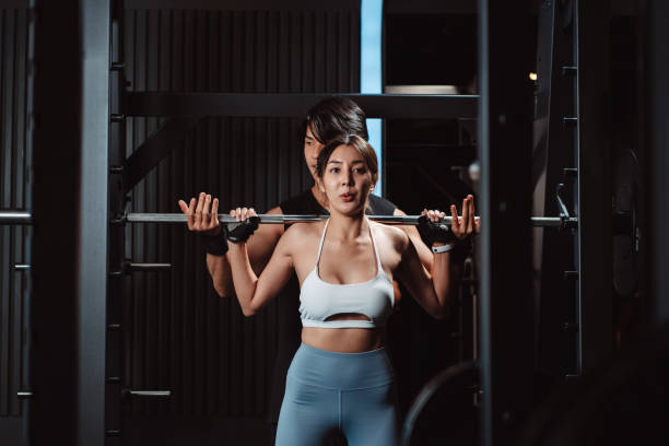 istock Woman working out Bodybuilder with coaching assistance to support weights at the gym. bodybuilder doing exercises with barbell. training sport healthy lifestyle bodybuilding. 1477871955
