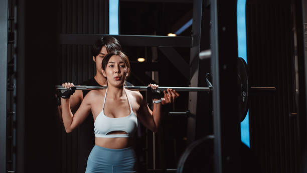 istock Woman working out Bodybuilder with coaching assistance to support weights at the gym. bodybuilder doing exercises with barbell. training sport healthy lifestyle bodybuilding. 1477873568