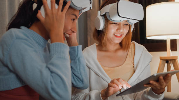 primer plano de jóvenes parejas lesbianas asiáticas influyentes usando auriculares de realidad virtual vr divirtiéndose bailando música de moda juntos en la sala de estar de su casa por la noche. bailar y cantar en una habitación acogedora. - sofa music teenager friendship fotografías e imágenes de stock