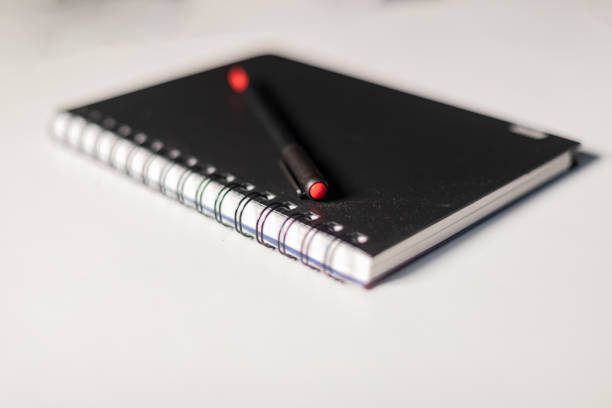 Black cover spiral binding notebook with a pen on it isolated on white background