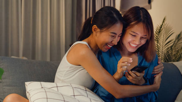 istock Young Asian lesbian couple ladies having fun use smartphone device do e-shopping on internet on sofa couch together in living room at home at night. Pride month, Lifestyle Pride Month. 1477877507