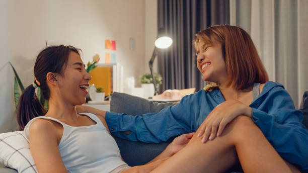 istock Young Asian lesbian couple ladies having fun while talking about something funny and relaxing on sofa couch together in living room at home at night. Pride month, Lifestyle Pride Month. 1477877559