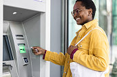 A young African American woman is inserting a debit card into an ATM