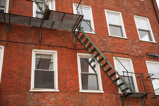 view of fire escapes on buildings and houses. A series of metal ladders and platforms are visible on the exterior walls of the structures. Captures the urban aesthetic of the fire escape.