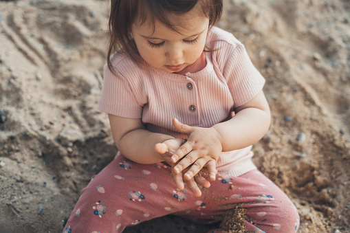 Caucasian child playing on sandy ground outdoor with cute fac, enjoying in relaxing day. Family activity in summer, freedom concept.