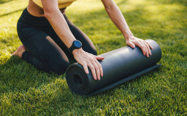 Body part of a woman in sport costume sitting and rolling up the yoga mat. Yoga and pilates concept. People body fit healthy. Sitting woman outdoors. Fitness woman. Healthy lifestyle, sport. parte del cuerpo de una mujer en traje deportivo sentada y enrollando la esterilla de yoga. concepto de yoga y pilates. el cuerpo de las personas se ajusta saludablemente. mujer sentada al aire libre. mujer fitness. estilo de vida saludable, deporte.