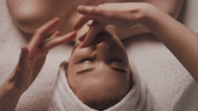 Beautiful woman with closed eyes relaxing in spa salon getting face massage in beauty spa. Serene woman relaxing in a beauty center. Professional beauty salon.