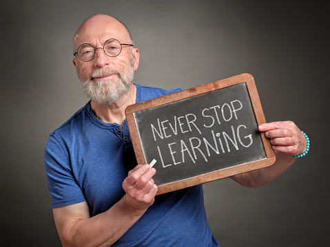 Never stop learning - motivation note on a slate blackboard held by a senior man, teacher, mentor or presenter, education, business and personal development concept communication concept