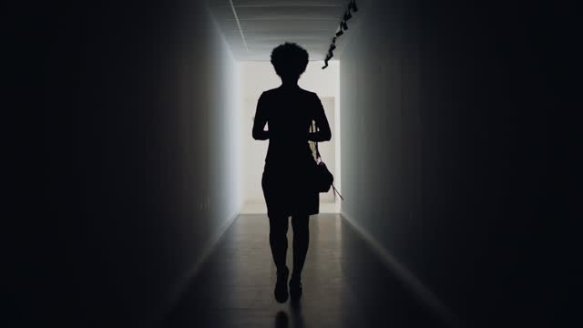 Silhouetted businesswoman walking along a dark corridor to an elevator