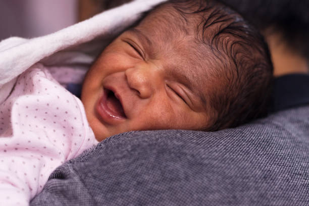 istock Cute little newborn baby curled up sleeping and smiling expression on shoulder with a white blanket 1477892990