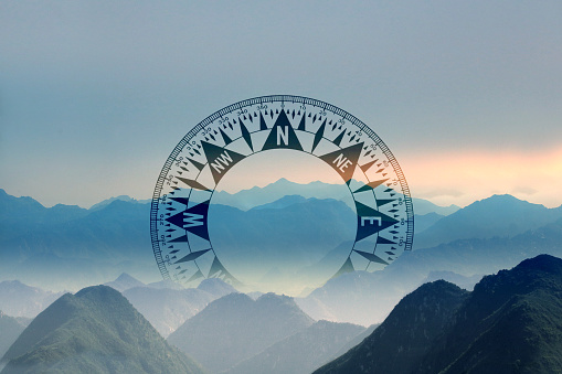 A compass sits nestled among one of the many valleys of a dramatic scene of overlapping mountain ridge lines.