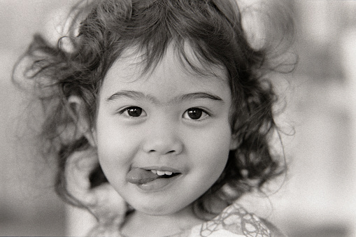 A black and white 35mm film scan of a three year old multiracial girl making a silly face.