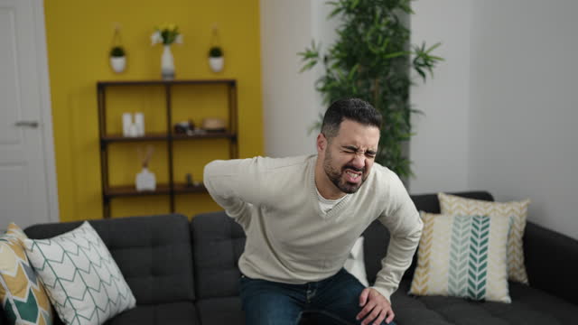 Young hispanic man suffering for backache sitting on sofa at home