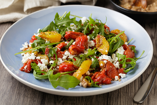 close view of roasted bell pepper, rocket leaves salad with walnut dressing and feta cheese flakes