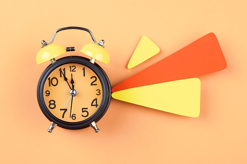 Alarm clock and papers on orange background. The clocks time is showing 5 to 12.