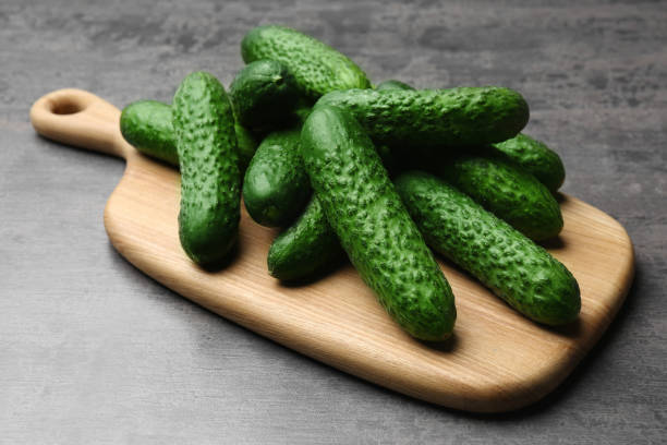 istock Wooden board with fresh ripe cucumbers on dark grey table 1477902604