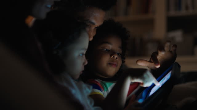happy family using tablet computer with children mother and father watching movie with kids on touchscreen technology enjoying relaxing evening before bedtime