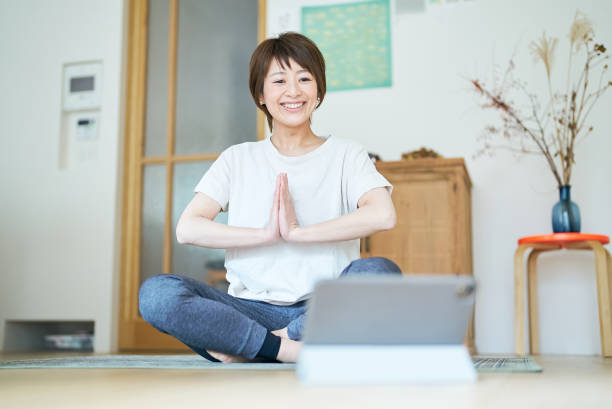 una donna che si allunga mentre guarda lo schermo di un tablet pc - yoga business women living room foto e immagini stock