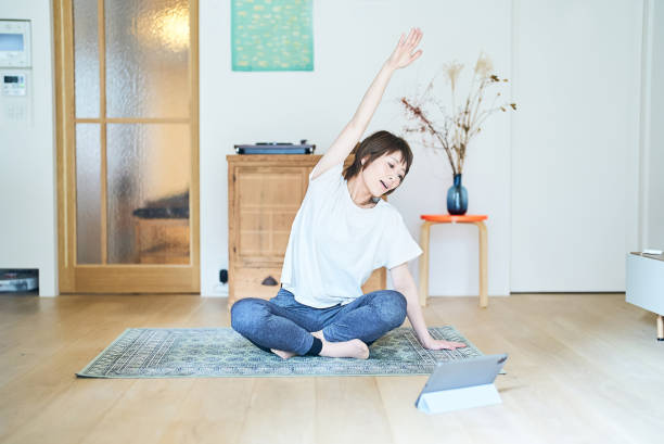 una donna che si allunga mentre guarda lo schermo di un tablet pc - yoga business women living room foto e immagini stock