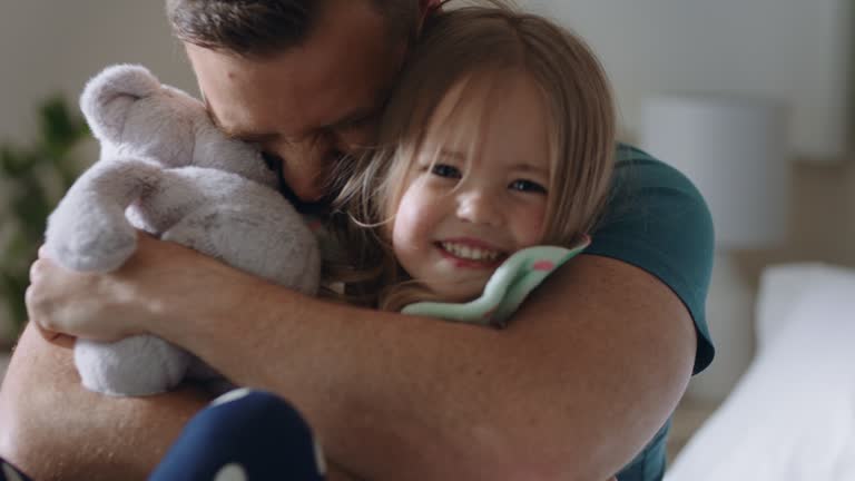 happy father hugging daughter in bed little girl laughing enjoying hug from dad loving parent embracing child having fun weekend morning at home