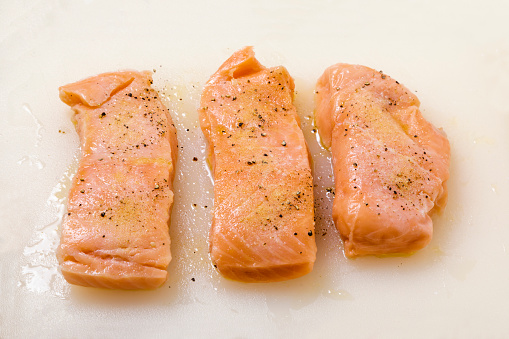 Three salmon fillets seasoned with salt, pepper and garlic powder on a white surface