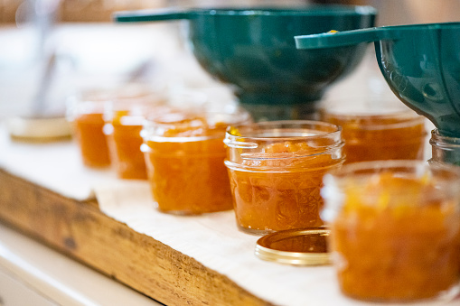 This is a photograph of sterilized glass jars filled with homemade mango jam with plastic funnels on the kitchen countertop.