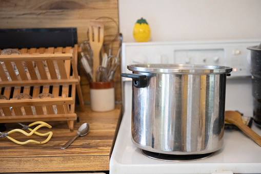 This is a photograph of a large stainless steel cooking pot boiling water on the stovetop in a real kitchen.