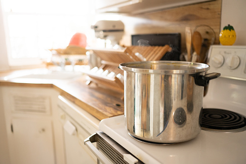 This is a photograph of a large stainless steel cooking pot boiling water on the stovetop in a real kitchen.