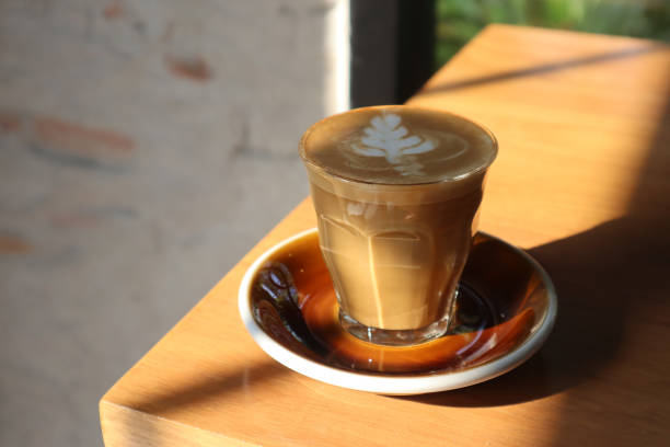 Flat white coffee in crystal glass on wooden table.