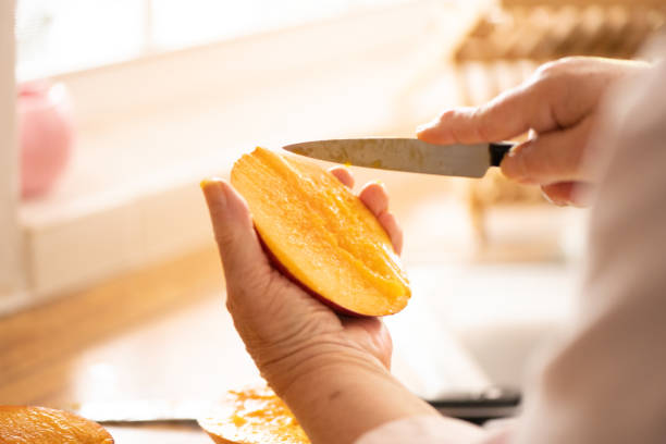This is a photograph with a shallow depth of field of    the hands of an unrecognizable senior woman holding a fresh sliced mango at home.