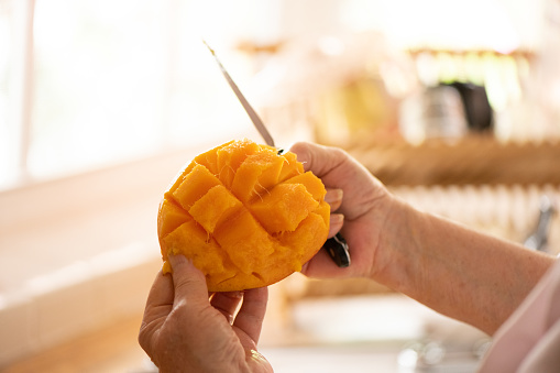 This is a photograph with a shallow depth of field of    the hands of an unrecognizable senior woman holding a fresh sliced mango at home.