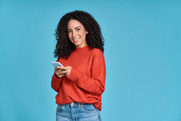 istock Young smiling latin woman using mobile phone isolated on blue background. 1477941164
