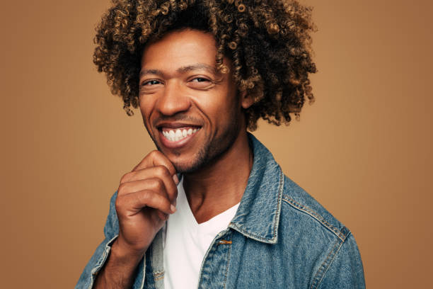 istock Delighted young black guy touching chin and smiling in brown studio 1477941268