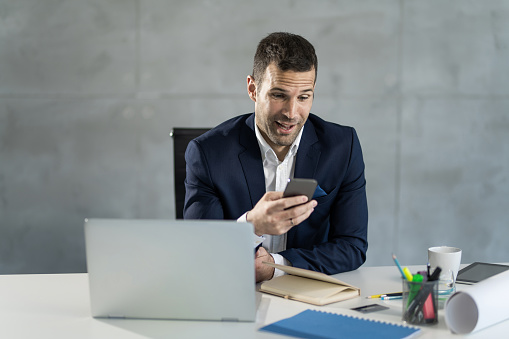 Surprised mid adult male entrepreneur checking emails on smart phone in the office.