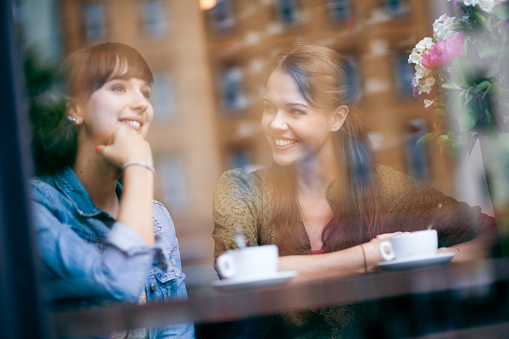 Young women sitting in cafe, smiling. Very shallow depth of field, image taken through the cafe window.