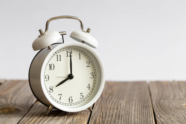 istock White alarm clock on a wooden surface close-up, blurred white background. 1477961502