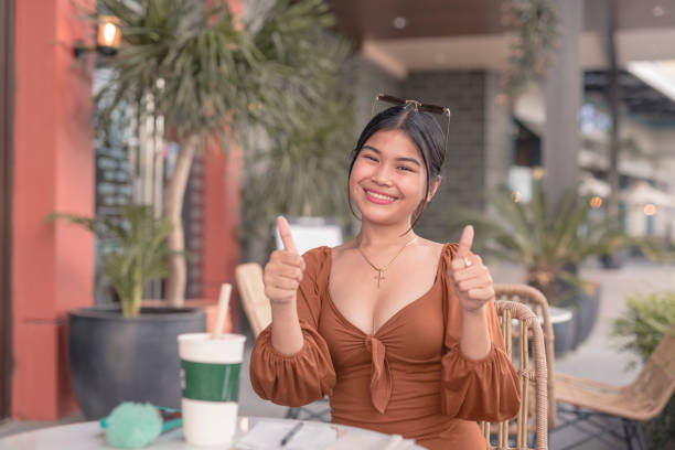 uma jovem sorridente posa para a câmera enquanto segura dois polegares do lado de fora do café. - puffed sleeve - fotografias e filmes do acervo