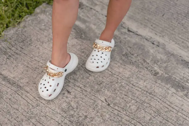 Photo of Putting on a comfy and stylish white sandals with gold chains design. Wearing the new and fashionable footwear style made from rubber material.