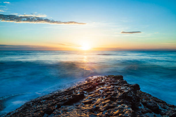 istock Bright sunrise over the ocean, with waves washing over rocks 1477967306