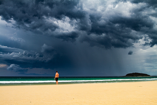 Man standing on beach with dark dramatic storm cloud and rain coming
