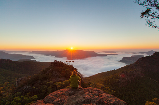 Young man enjoying the view on top of a mountain at sunrise, NSW, Australia.