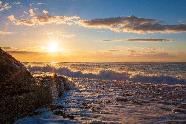 Bright sunrise over the ocean, with waves washing over rocks
