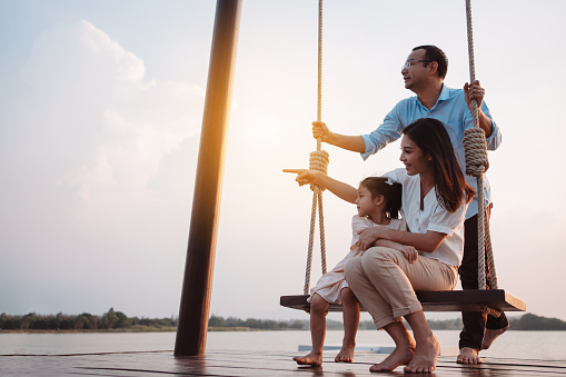 Happy family enjoying with swing in the park at sunset outdoor in nature, Weekend activity of family life together.