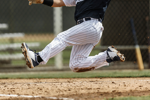 Baseball player, running at full speed, begins his slide into home plate, high off of the ground, no face shown in photograph