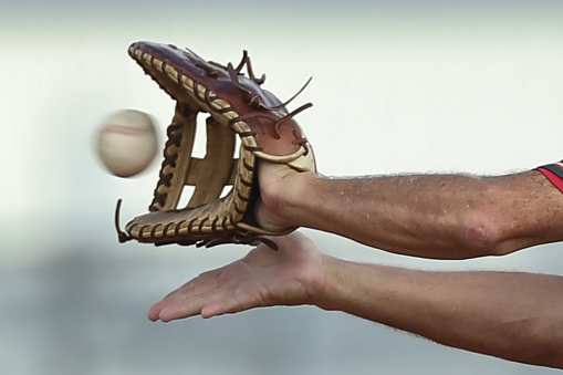 Baseball milliseconds away from being caught by the first baseman, no faces shown in photograph, closeup, arms, hands, baseball and first baseman's glove