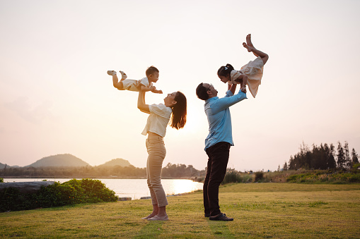 Happy family in the park sunset light. family on weekend playing together in the meadow with river Parents hold the child and daughter hands.health life insurance plan concept.